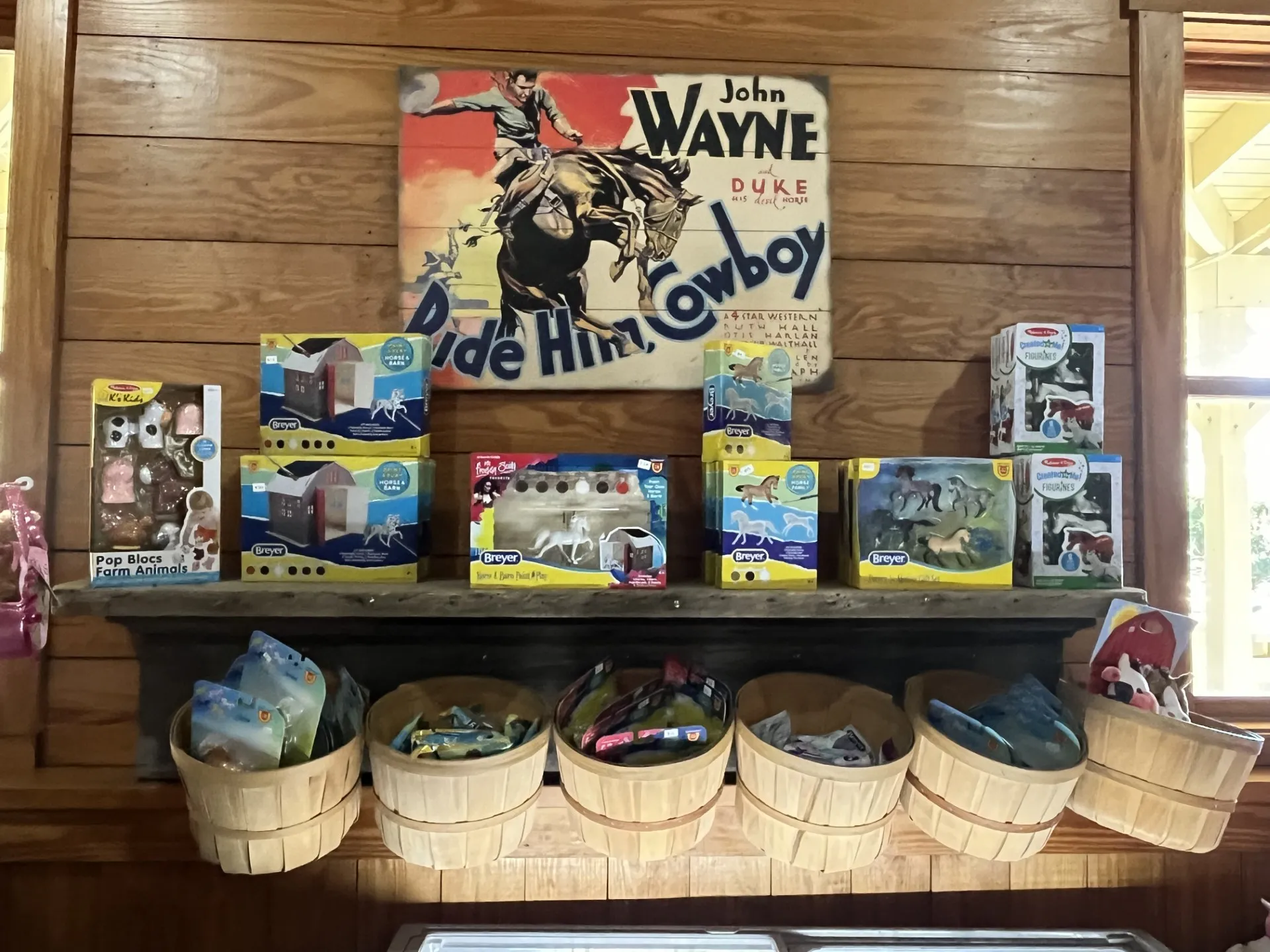 Wooden shelf with toy animal sets and baskets below, with vintage cowboy poster on the wall.