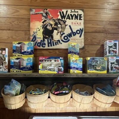 Wooden shelf with toy animal sets and baskets below, with vintage cowboy poster on the wall.