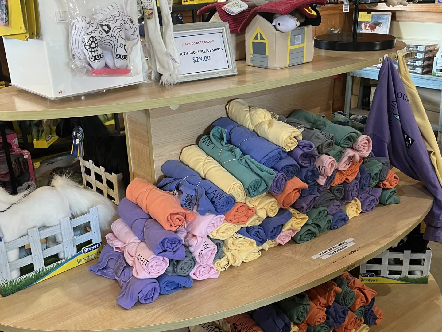 Store display with rolled shirts, mini coloring kits, plushies, and toy horses.
