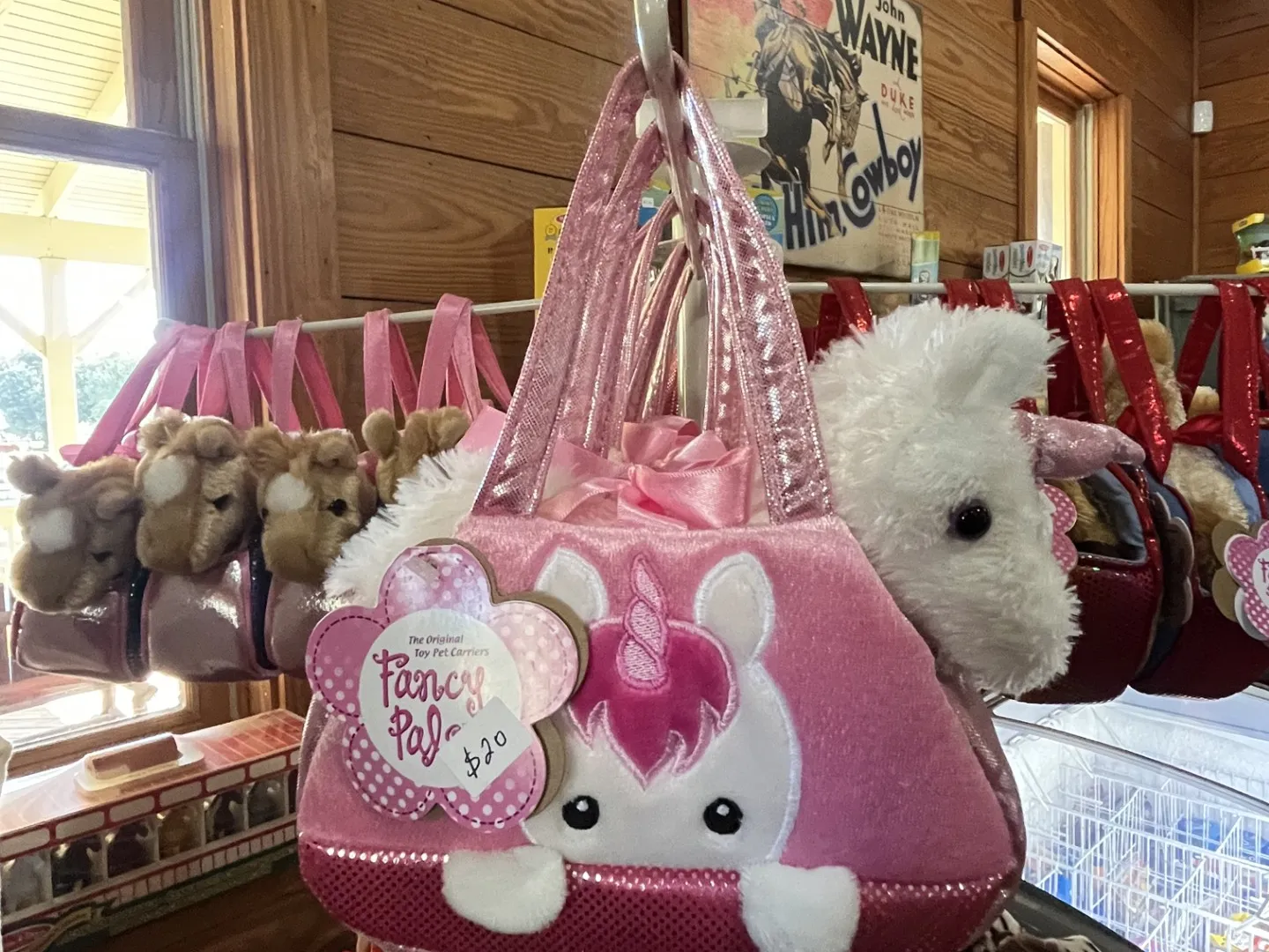 Pink unicorn-themed plush purse with animal toys in a wooden store setting.