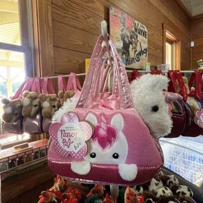 Pink unicorn-themed plush purse with animal toys in a wooden store setting.