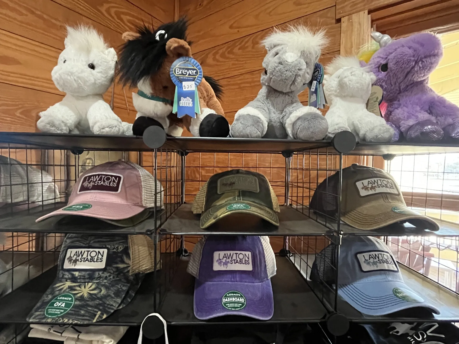 Stuffed animals on top shelf, hats with 'Lawton Stables' logo on lower shelves.