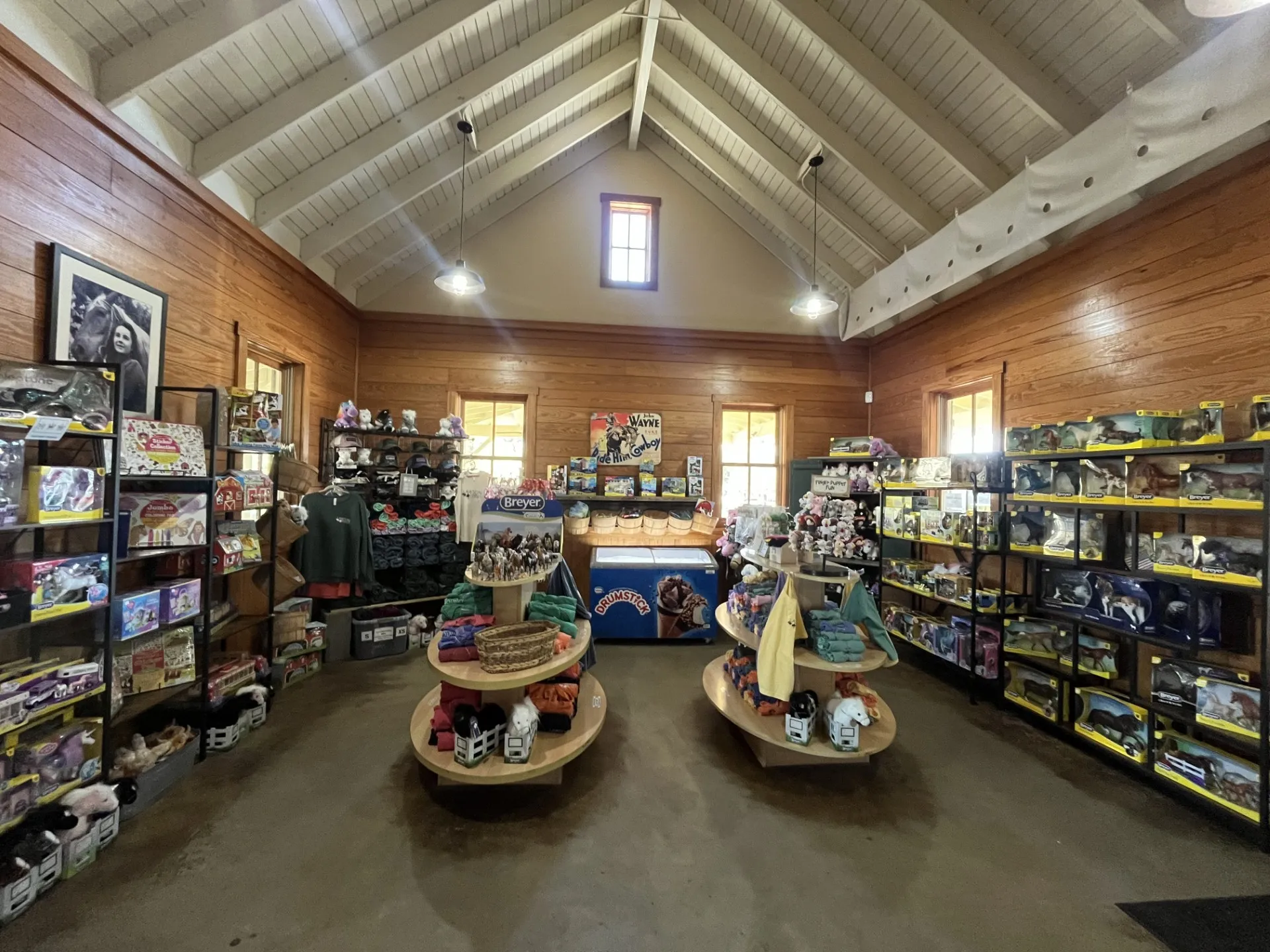 Wooden gift shop interior with toys and clothing on shelves and tables.